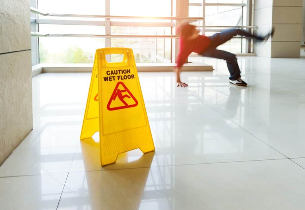 Man slips on wet floor after ignoring wet floor warning sign.